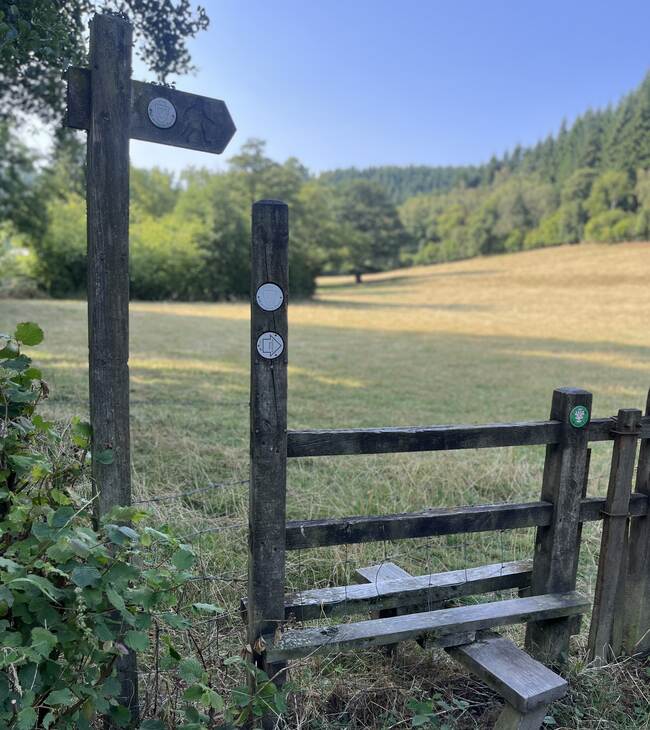 A wooden stile and footpath signpost on a walk from The Salwey Lodge near Ludlow