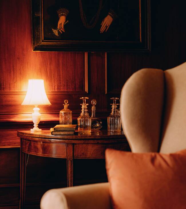 A glowing lamp and wing chair in a panelled room at The Salwey Lodge
